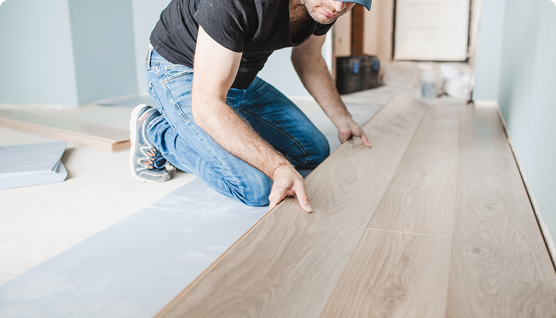 Man installing wooden flooring in a room.