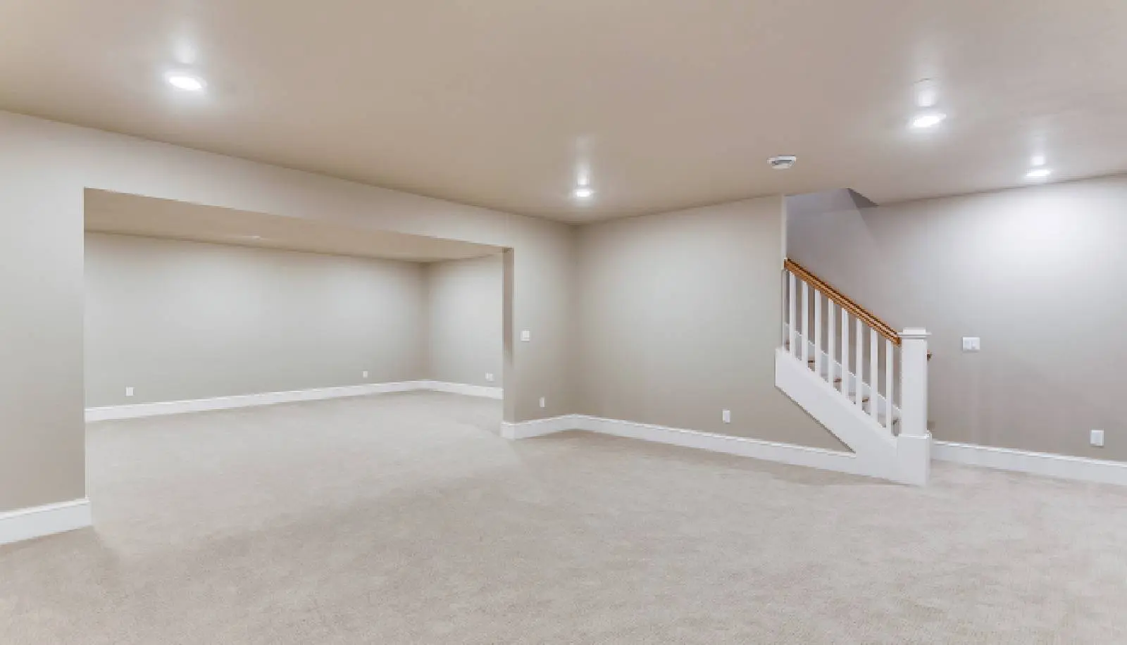 Empty basement room with beige carpet and white walls.